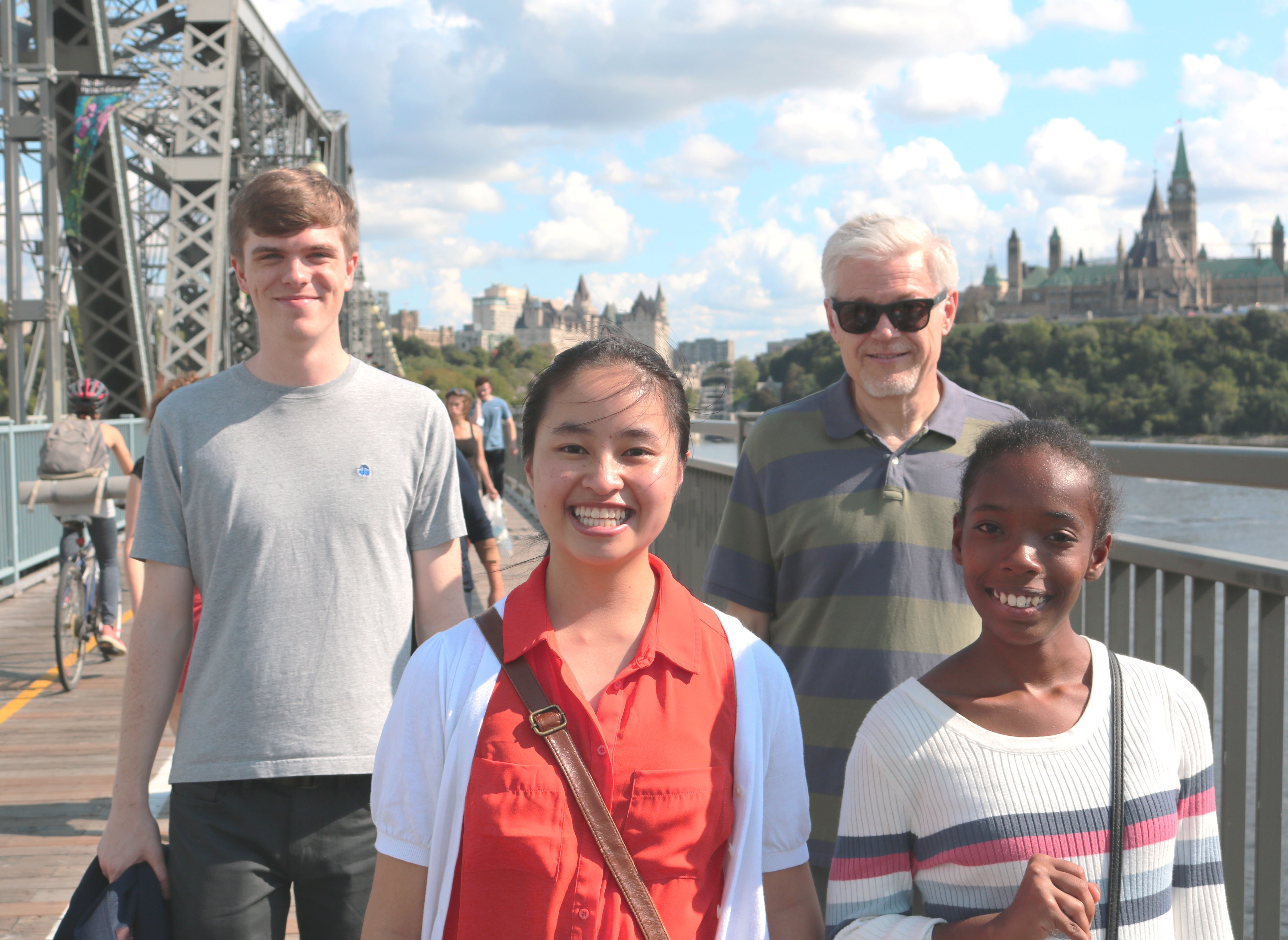 A group of people stands on a bridge in front of a large building on the opposing river bank.